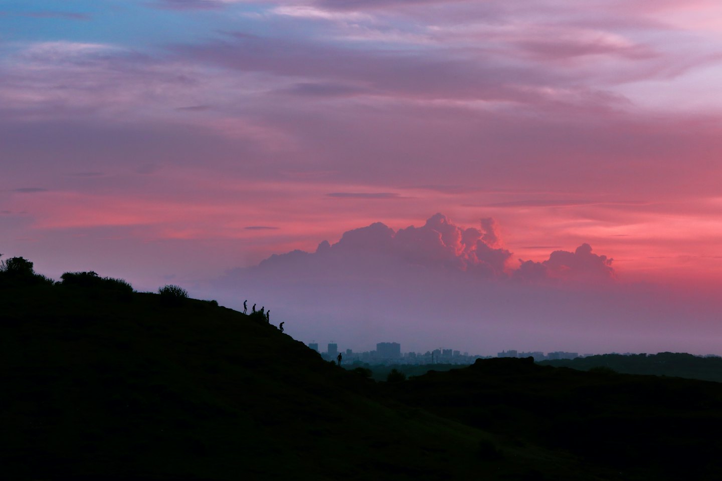 Hikers stand on a hill looking at a distant city skyline.