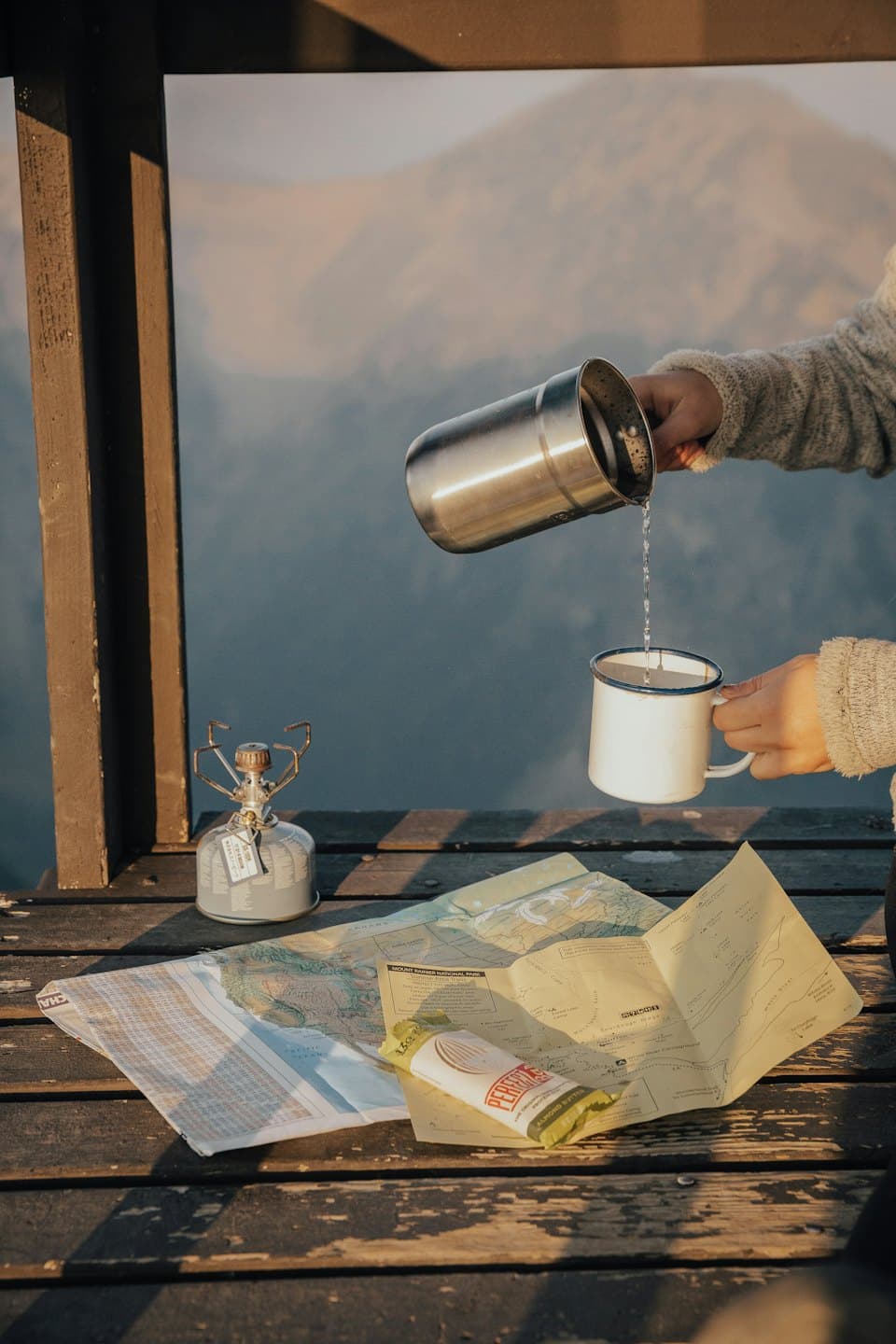 Hands pour hot water from a thermos into a mug during a hiking break.