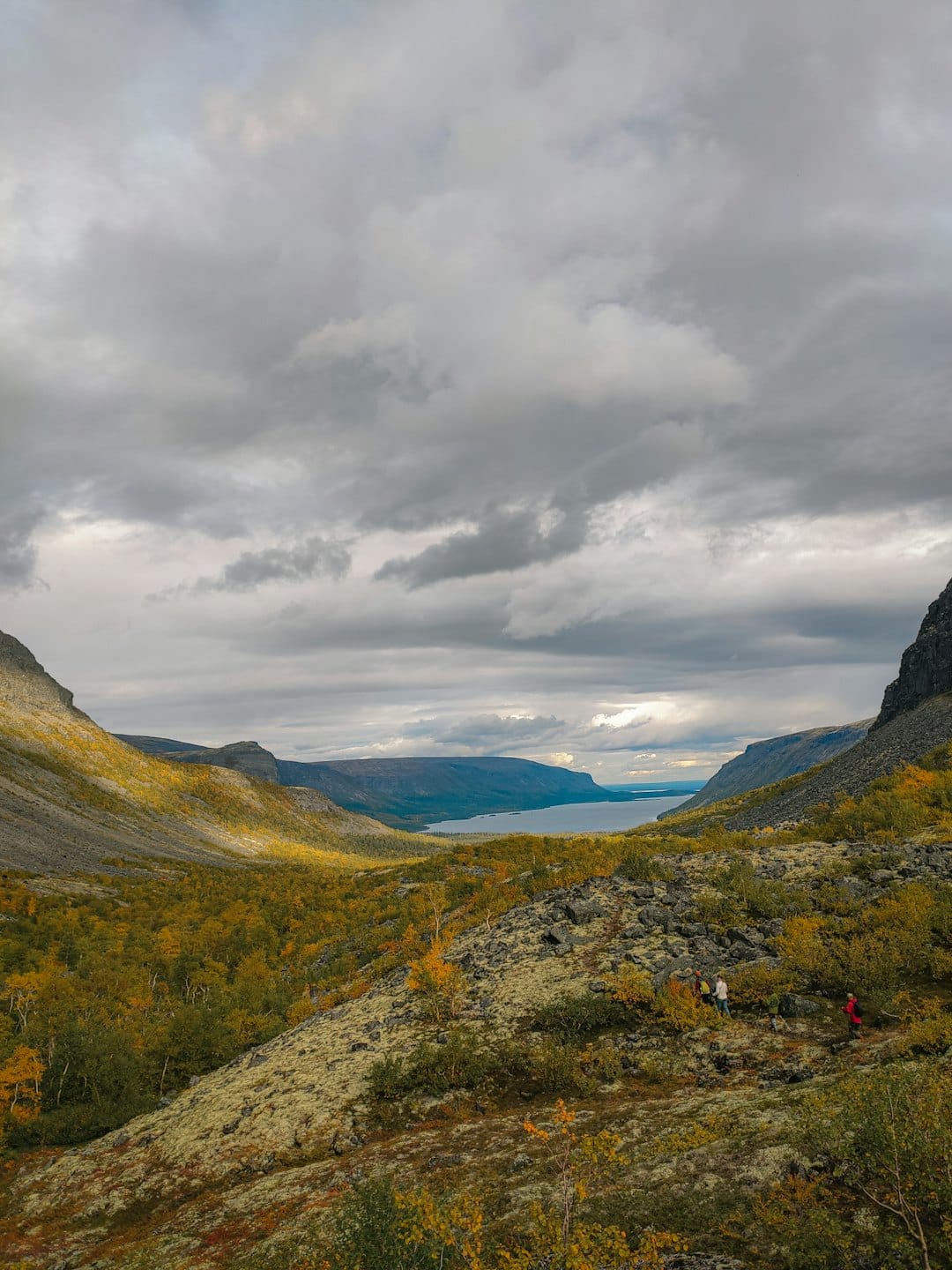 Hikers descending a rocky trail with autumn leaves.